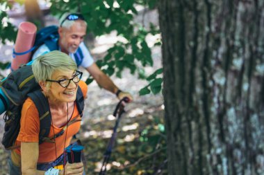 Mature couple hiking in forest wearing backpacks and hiking poles. Nordic walking, trekking. Healthy lifestyle.