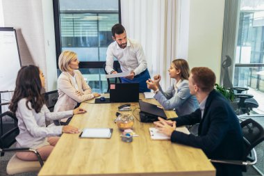 Office colleagues having discussion during meeting in conference room. Group of men and women sitting in conference room and smiling.