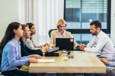 Office colleagues having discussion during meeting in conference room. Group of men and women sitting in conference room and smiling.
