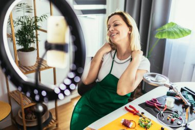Genç bayan aksesuar tasarımcısı stüdyo atölyesinde el yapımı mücevherler yapıyor ve video kaydediyor. Moda, yaratıcılık ve el yapımı konsept.