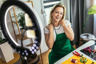 Genç bayan aksesuar tasarımcısı stüdyo atölyesinde el yapımı mücevherler yapıyor ve video kaydediyor. Moda, yaratıcılık ve el yapımı konsept.