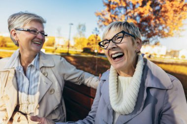 Two senior female friends sitting on the bench in the park
