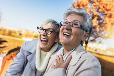 Two senior female friends sitting on the bench in the park