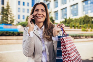 Şehirde alışveriş yaparken cep telefonunu kullanan çekici genç bir kadın.