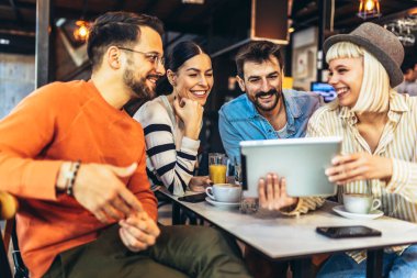 Young friends looking at digital tablet while sitting in cafe. Young people having a great time in cafe.
