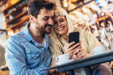Kafede akıllı telefon kullanan mutlu genç çift.