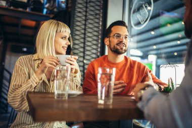 Young people have a great time in a cafe. Friends sitting in a coffee shop, drinking coffee, and having fun together.