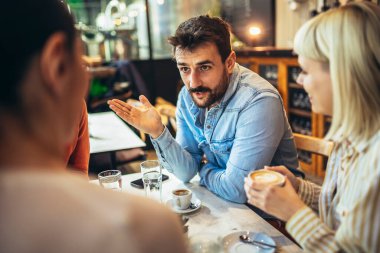 Young people have a great time in a cafe. Friends sitting in a coffee shop, drinking coffee, and having fun together.