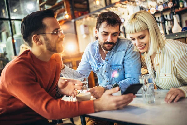 Young people have a great time in a cafe. Friends sitting in a coffee shop, using phones, drinking coffee, and having fun together.