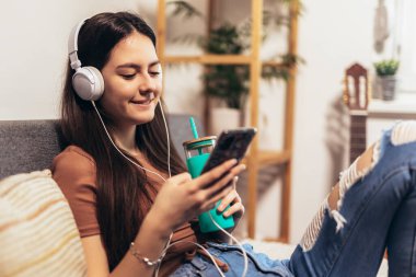Beautiful teenager girl surfing social media on smart phone while having leisure time at her home.