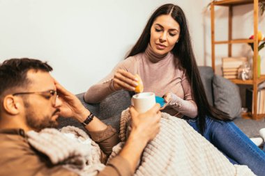 Sick young couple drinking hot tea at home - health, flu and people concept 