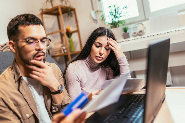 Молодая пара оплачивает счета вместе, клиенты платят кредитной картой онлайн, сидя в уютной гостиной на дому