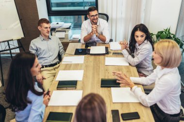 Office colleagues having discussion during meeting in conference room. Group of men and women sitting in conference room and smiling.