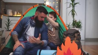 Baba ve oğul oturma odalarında kamp çadırlarıyla eğleniyorlar..