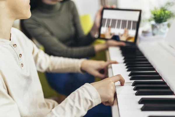 Brother and sister play electric piano at home and have fun. The sister helps her younger brother to play piano.They use a digital tablet for online lessons.