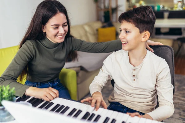 Brother and sister play electric piano at home and have fun. The sister helps her younger brother to play piano