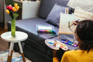 Preteen girl is using a paintbrush to bring creativity and color to life on a table, creating an indoor flower masterpiece.