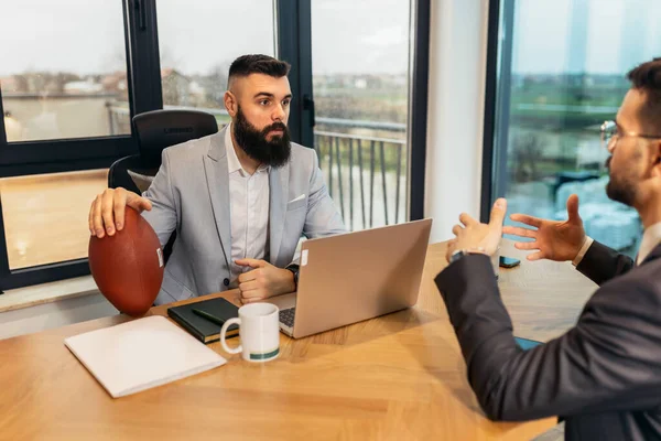 stock image Handsome young businessman holding a rugby ball in the office when talking with his colleague