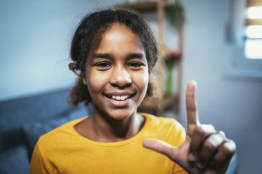 Beautiful smiling black deaf girl using sign language at home