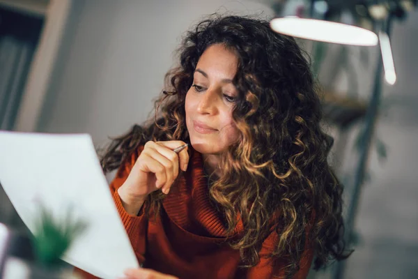 Woman holding papers in her hands, calculating family budget at home.