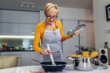 Modern mutfağında yemek pişiren son sınıf mutlu bir kadın.