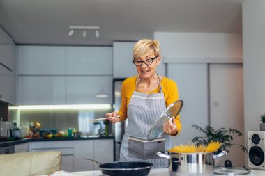 Modern mutfağında yemek pişiren son sınıf mutlu bir kadın.