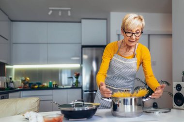 Modern mutfağında yemek pişiren son sınıf mutlu bir kadın.