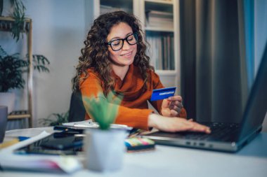 Kadın evde oturuyor, elinde kredi kartı tutuyor internetten sipariş veriyor ya da internetten alışveriş yapıyor..