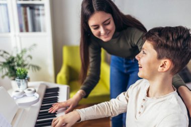 Brother and sister play electric piano at home and have fun. The sister helps her younger brother to play piano