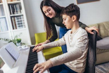 Brother and sister play electric piano at home and have fun. The sister helps her younger brother to play piano