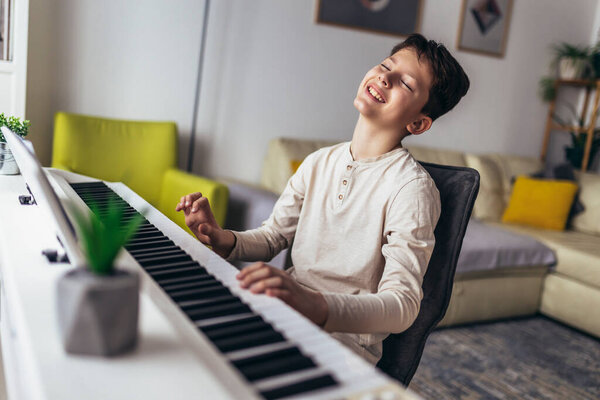 Little boy playing piano in living room. Child having fun with learning to play music instrument at home.