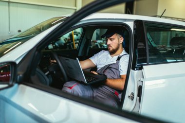 Professional car mechanic working in auto repair service using laptop. clipart