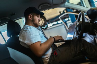 Profesyonel araba tamircisi dizüstü bilgisayar kullanarak oto tamir servisinde çalışıyor..