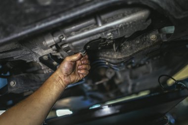 Benzin istasyonunda asansörde asılı duran arabanın yanında profesyonel biri var.