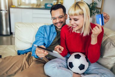 Genç çift dijital tabletten futbol maçı izliyor ve online bahis için kredi kartı kullanıyorlar..