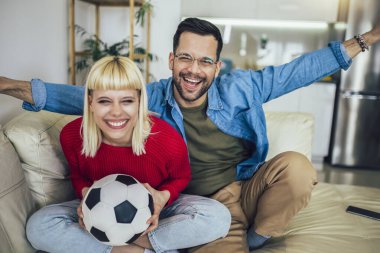 Genç bir çift evlerinin rahatlığından televizyonda futbol maçı izliyor..