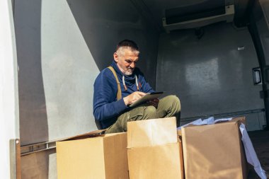 Kamyon şoförü kargo aracının arkasında dururken dijital tablette sevkiyat listesini kontrol ediyor..