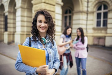 Öğrenci, arkadaşları onun arkasında çalışırken not defteriyle ayakta duruyor.