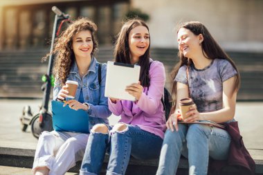 Bir grup kolaj kızı bankta oturup okula çalışıyor.