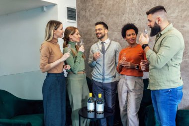 Group of  businesspeople sitting together in a co-working space and celebrating with alcohol drink.
