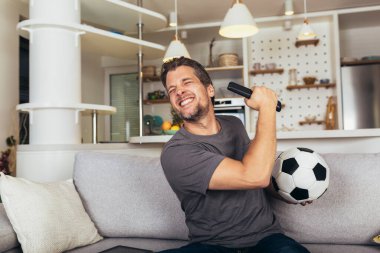 Genç futbol fanatiği oturma odasındaki kanepede futbol maçı izliyor..