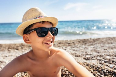 Portrait of a smiling boy on the beach with a straw hat.
