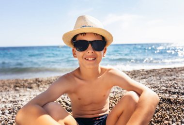 Portrait of a smiling boy on the beach with a straw hat.