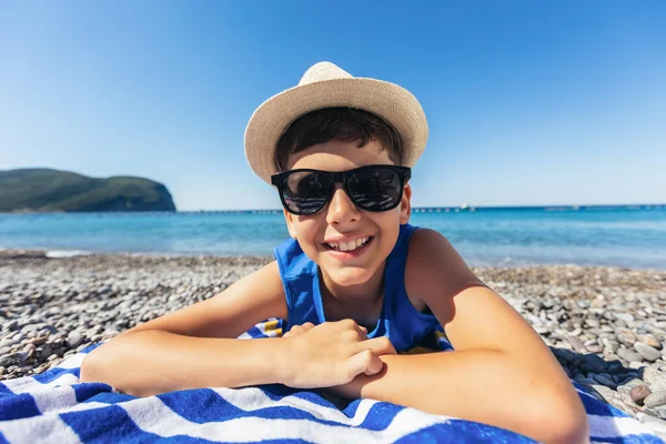 Het Jongetje Ligt Een Gestreepte Blauwe Witte Strandhanddoek Glimlacht Vrolijk — Stockfoto