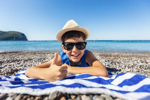 小男孩躺在一条蓝白相间的沙滩毛巾上 开心地笑着 — 图库照片