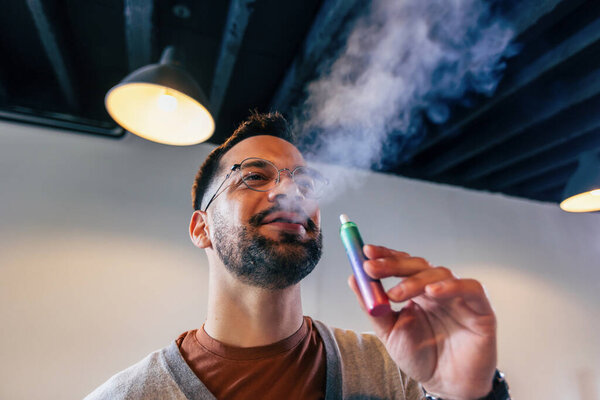 Young man smoking an electronic cigarette to quit tobacco. Vape man. Alternative nicotine-free smoking concept