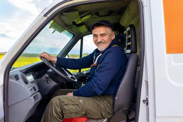 Portrait of a cheerful delivery driver looking out the window of the white cargo van vehicle, delivering goods by car