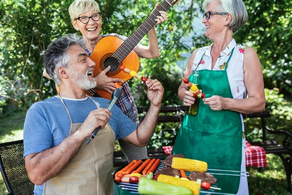 Group of elderly people enjoying their retirement by going on a picnic, playing a guitar and singing, making barbeque, making memories and making their friendship stronger