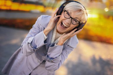 Sonbaharda renkli bir parkta kablosuz kulaklıkla müzik dinleyen yaşlı bir kadın.