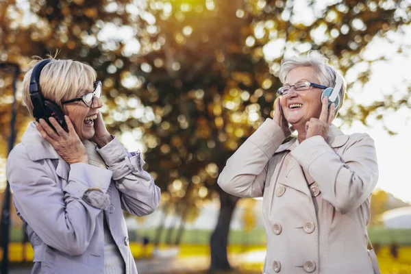 Dvě Starší Ženy Poslouchají Hudbu Bezdrátových Sluchátkách Barevném Parku Podzim — Stock fotografie